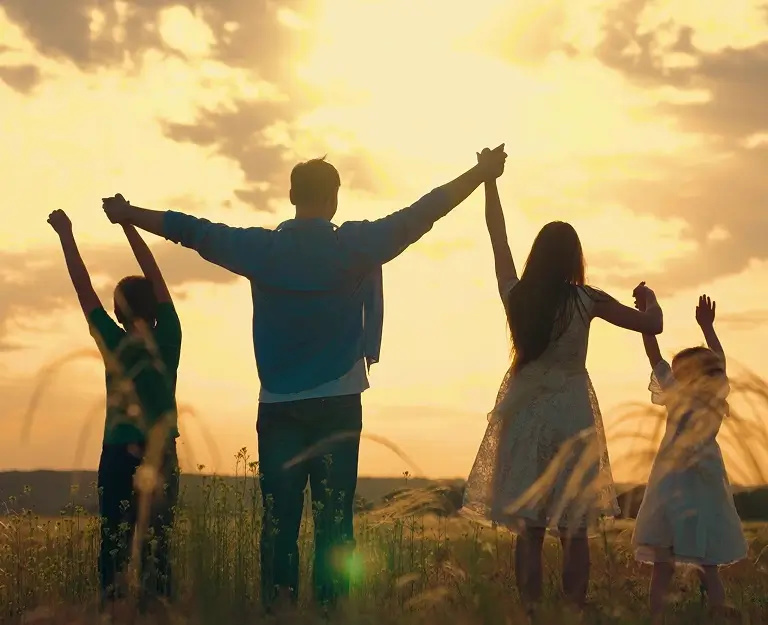 A joyful family poses in a field, arms lifted high, expressing happiness and togetherness in nature