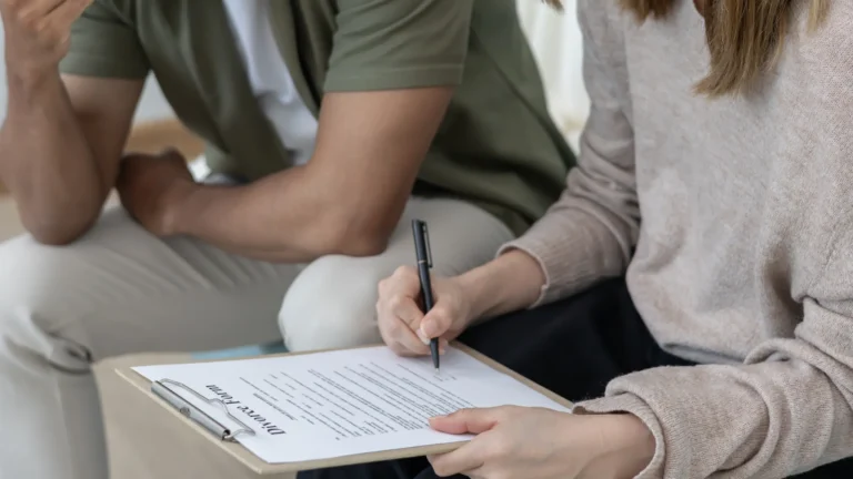 Two individuals reviewing and signing a divorce form on a clipboard indoors.