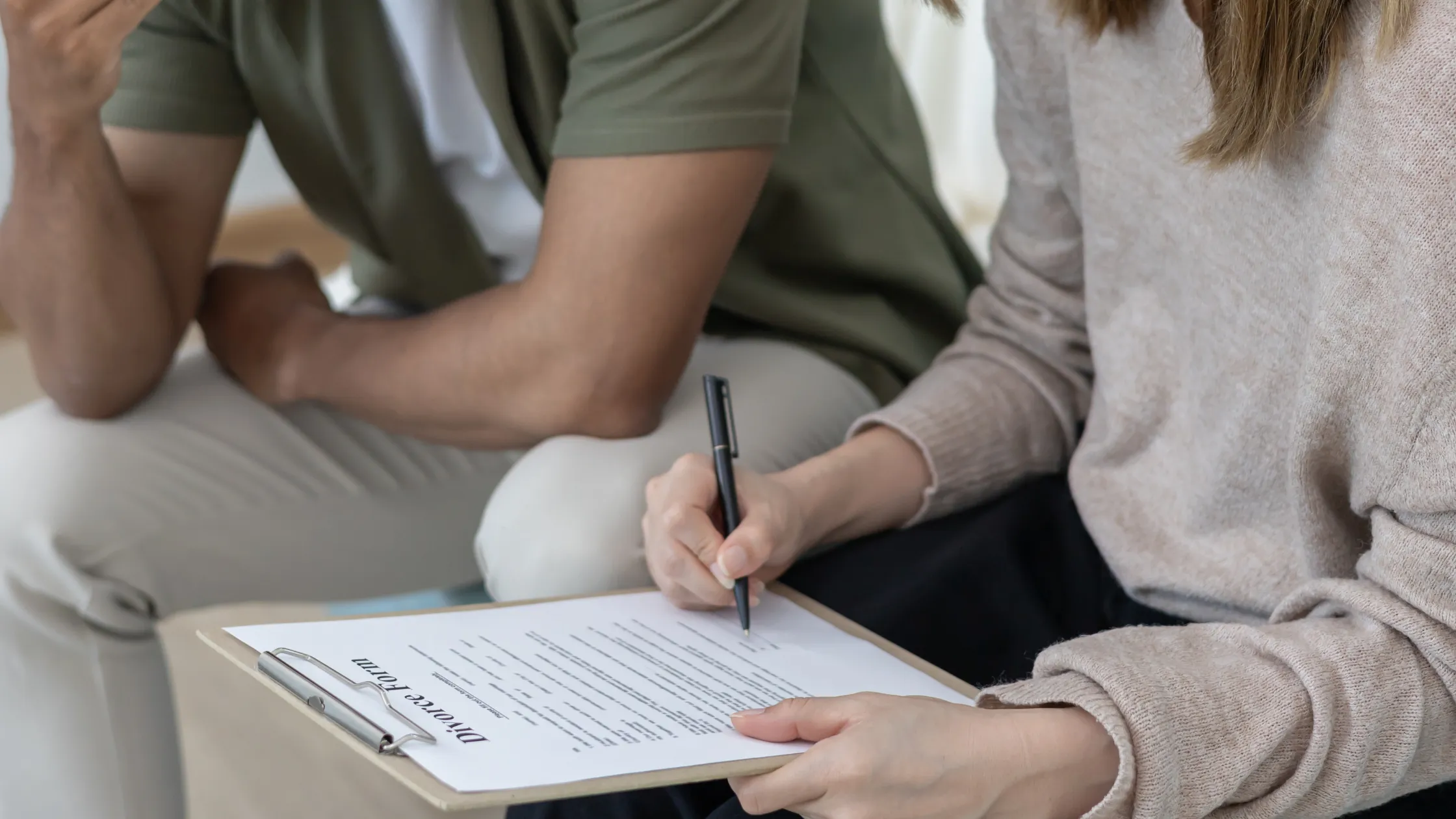 Two individuals reviewing and signing a divorce form on a clipboard indoors.