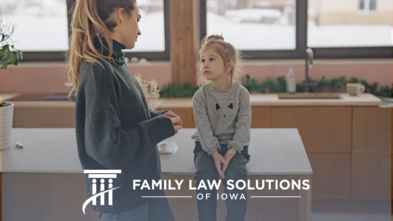 Woman in dark sweater talking to young girl in gray cat sweatshirt sitting on kitchen counter.