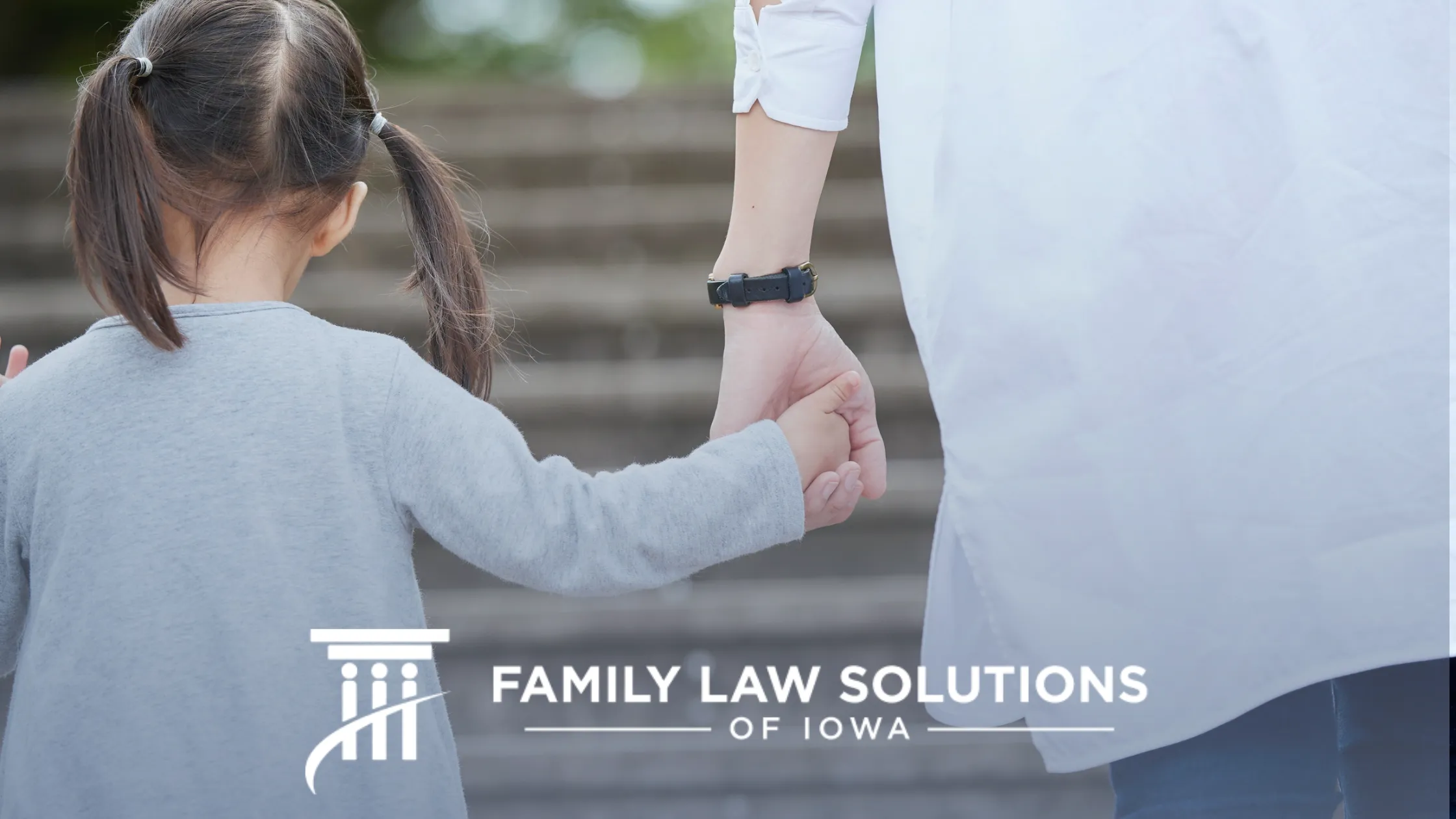 Adult and child holding hands walking up outdoor stone steps, with "Family Law Solutions of Iowa" text.